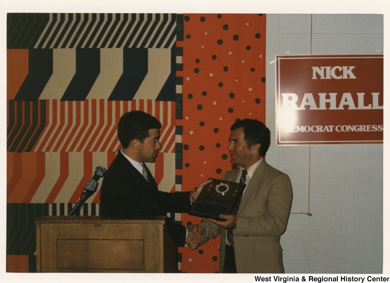 On the right, Representative Nick J. Rahall (D-W.Va.) shakes hands with an unidentified man and receives a plaque.
