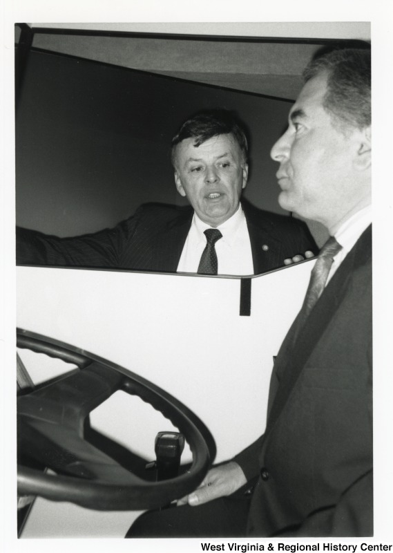 Representative Nick J. Rahall (D-W.Va.) sits behind the wheel of a vehicle while an unidentified man stands outside.