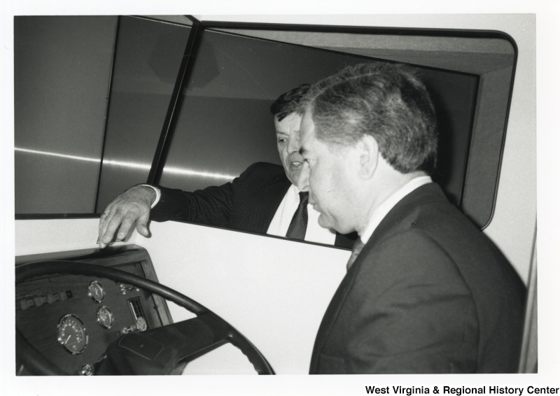 Representative Nick J. Rahall (D-W.Va.) sits behind the wheel of a vehicle while an unidentified man stands outside.