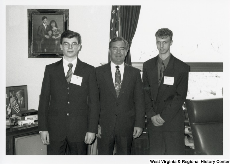 Congressman Nick J. Rahall (D-W.Va.) stands between two unidentified men in his office.