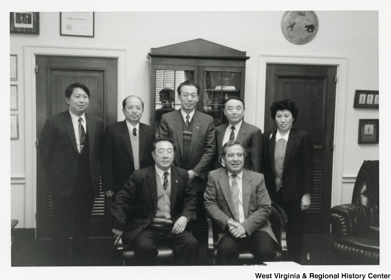 Representative Nick J. Rahall (D-W.Va.) sits in front of a group of six unidentified people for a photograph.