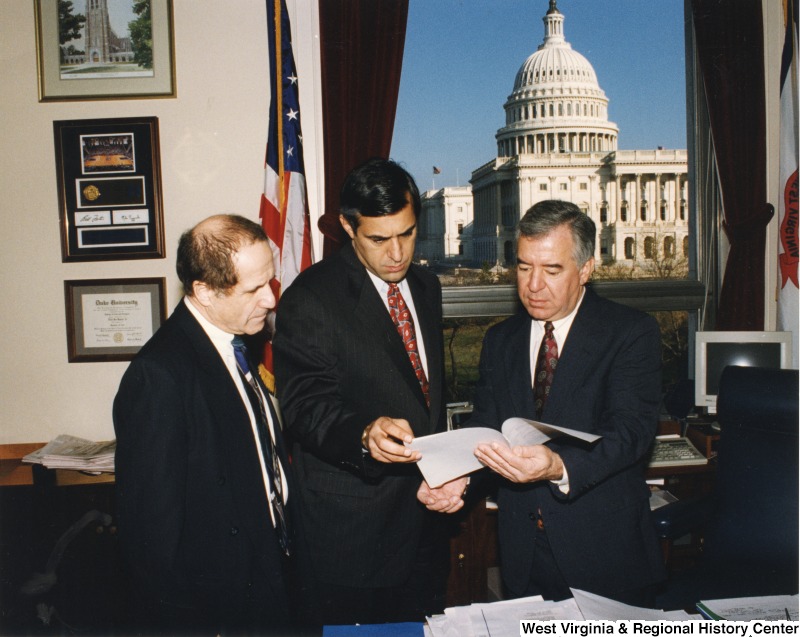 On the right, Representative Nick J. Rahall (D-W.Va.) looks over papers in his office with two unidentified men.