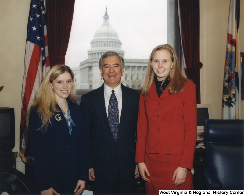 Representative Nick J. Rahall (D-W.Va.) stands for a photograph in his office between two unidentified women.
